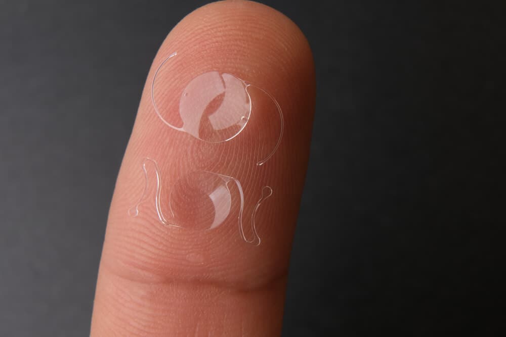 Transparente Kontaktlinse auf einer Fingerspitze vor dunklem Hintergrund.