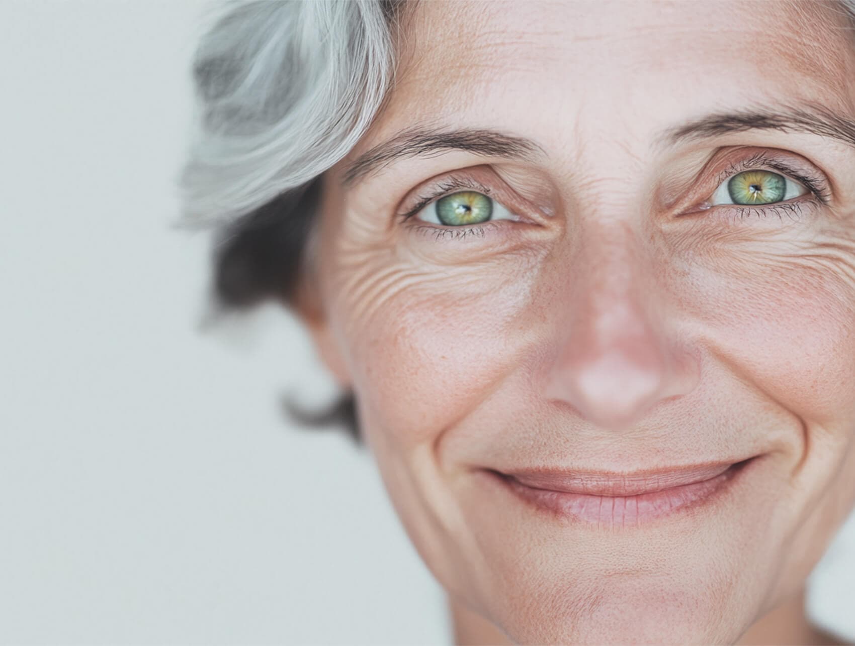 Nahaufnahme eines lächelnden Gesichts einer älteren Person mit grauen Haaren und grünen Augen, die ruhig und zufrieden wirkt.