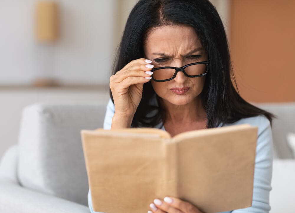 Alterssichtigkeit Presbyopie, Frau die ein Buch liest und eine Brille auf hat