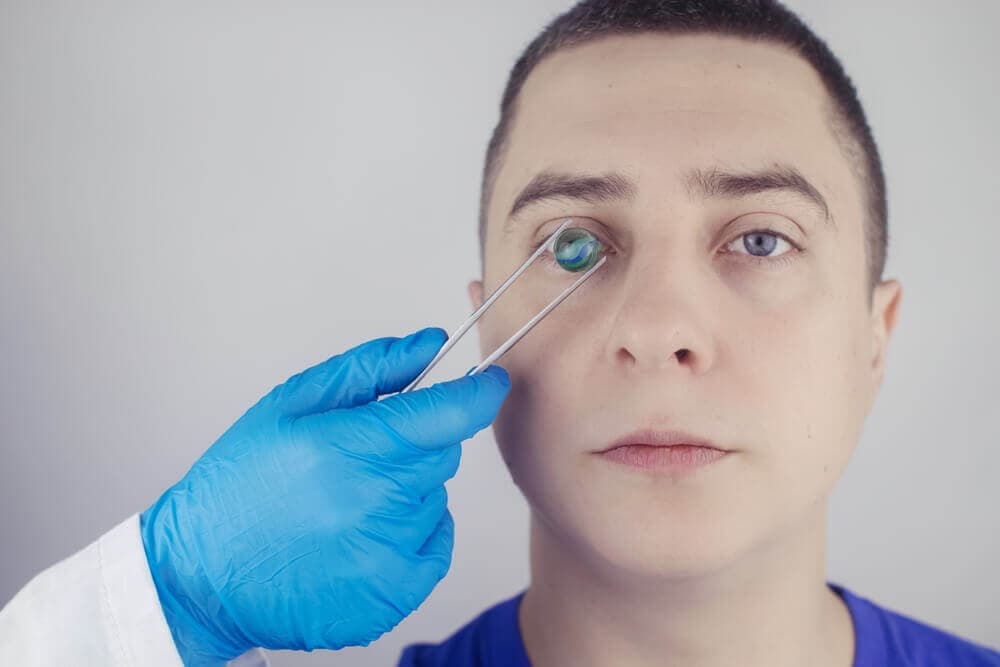 Arzt mit blauen Handschuhen hält optisches Gerät vor Auge eines Mannes.