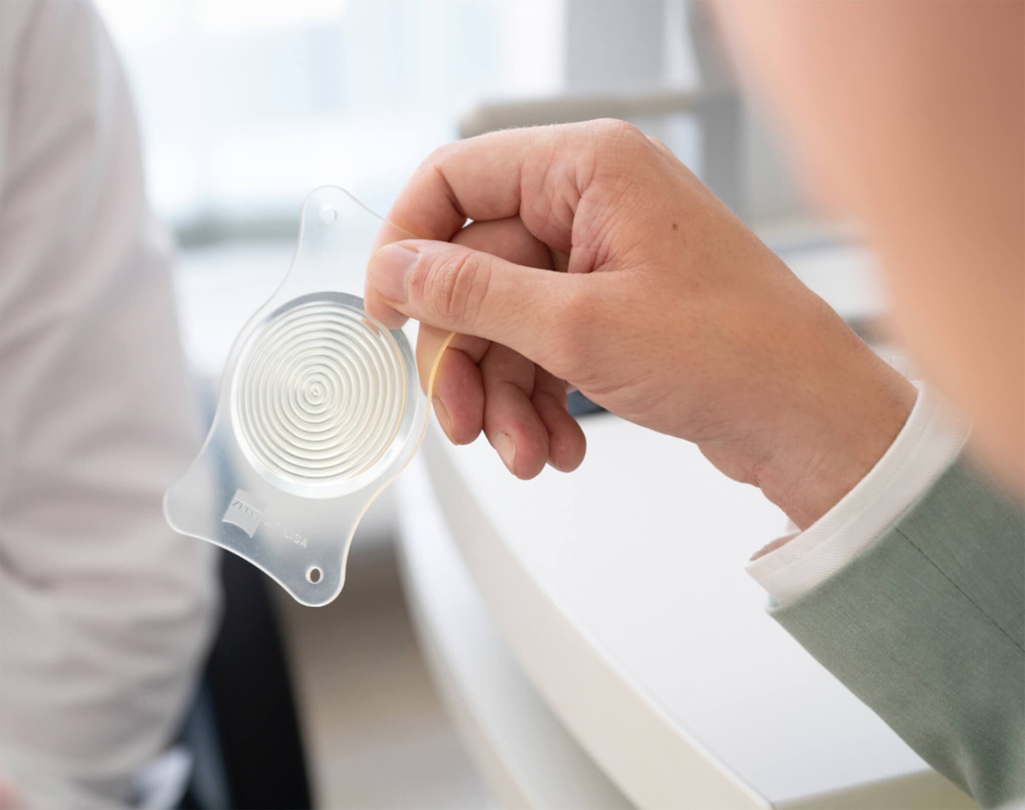 Hand hält transparentes Modell einer Augenlinse in einem Büro.