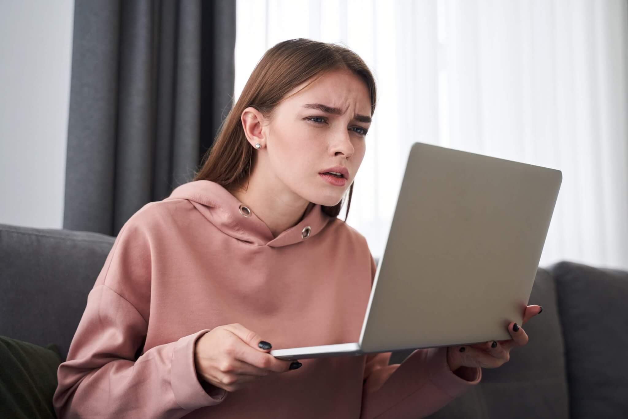 Junge Frau, die auf Laptop nichts erkennen kann, weil sie kurzsichtig ist