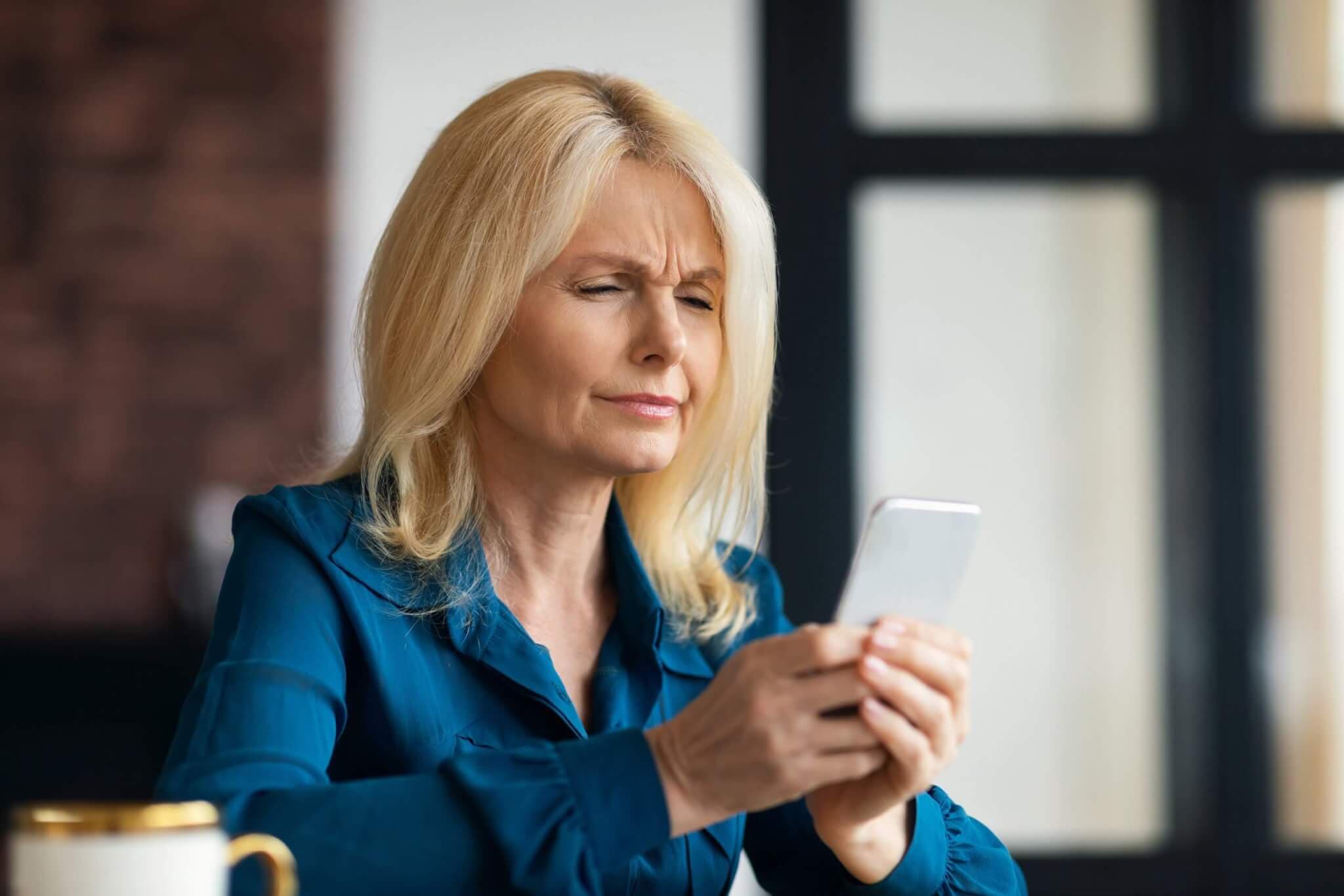 Frau mittleren Alters die an Presbyopie leide und den Text auf Ihrem Telefon nicht erkennen kann
